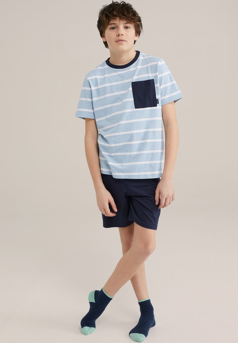 Lichtblauw gestreept T-shirt met korte mouwen en een marineblauwe zak, gecombineerd met marineblauwe shorts en marineblauwe sokken met muntgroene accenten.