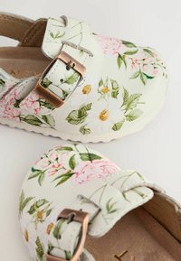 Weiß-blumige Clogs mit rosa Pfingstrosen und Gänseblümchen, einer strukturierten Oberfläche, zwei verstellbaren Schnallen und einer leichten, gepolsterten Sohle.