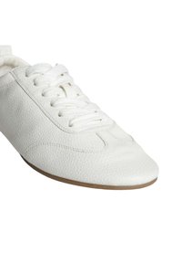 Baskets blanches en cuir avec une finition texturée, un bout arrondi et une semelle en caoutchouc plate. Elles présentent un laçage traditionnel et des détails de couture subtils.