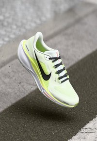 Chaussure de sport blanche et jaune fluo avec des accents noirs, tige en maille et semelle texturée. Dispose de lacets et d'une marque sur le côté.