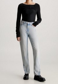 Černý top s dlouhým rukávem, kulatým výstřihem a zavíráním vpředu, v kombinaci se světle modrými vysokými džínami a černými platformovými botami.