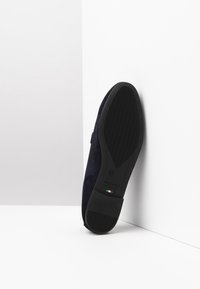 Scarpa di camoscio blu navy con suola in gomma nera testurizzata e accentuazioni. Presenta un lieve tacco e un design minimalista. Prodotta in Italia.