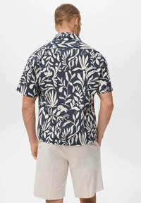 Camisa de manga corta en tela azul marino con patrones de hojas y flores en crema. Dobladillo recto con un ajuste holgado y cuello clásico.