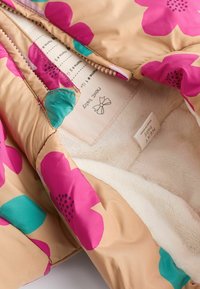 Chaqueta acolchada con un exterior beige que presenta grandes patrones florales en rosa y azul verdoso. Forrada con suave piel sintética blanca para mayor calidez.