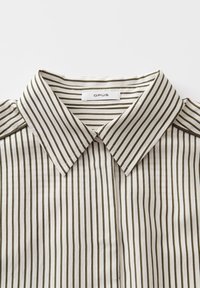 Camicia a righe color crema con sottili strisce verde scuro, con una trama tessuta e un'etichetta stampata all'interno del colletto.