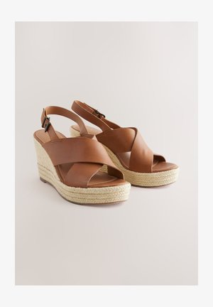 Pruunid nahast kiilkontsaga sandaalid risti rihmadega, avatud varbavahedega ja jute-mähisega platvormiga. Reguleeritav pahkluu rihm kindlaks kinnituseks.