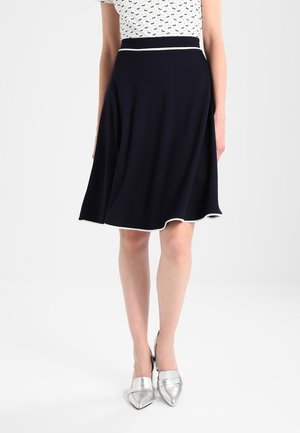 Vrouw die een zwarte knie-lange rok met witte rand draagt, gecombineerd met zilveren puntige schoenen en een witte top met zwarte hondenpatronen.