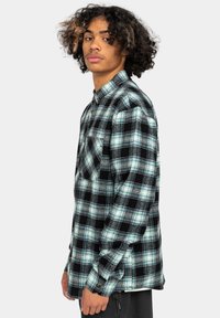 Rute flannel skjorte i sort, teal og hvid. Har en tryklås design, lange ærmer og en brystlomme. Blød tekstur hele vejen igennem.