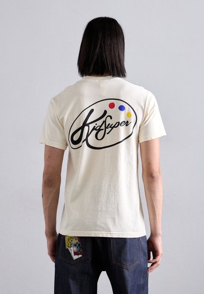 Crème-kleurige katoenen t-shirt met een zwart logo met kleurrijke stippen op de achterkant. Eenvoudig ontwerp, korte mouwen en een comfortabele pasvorm.