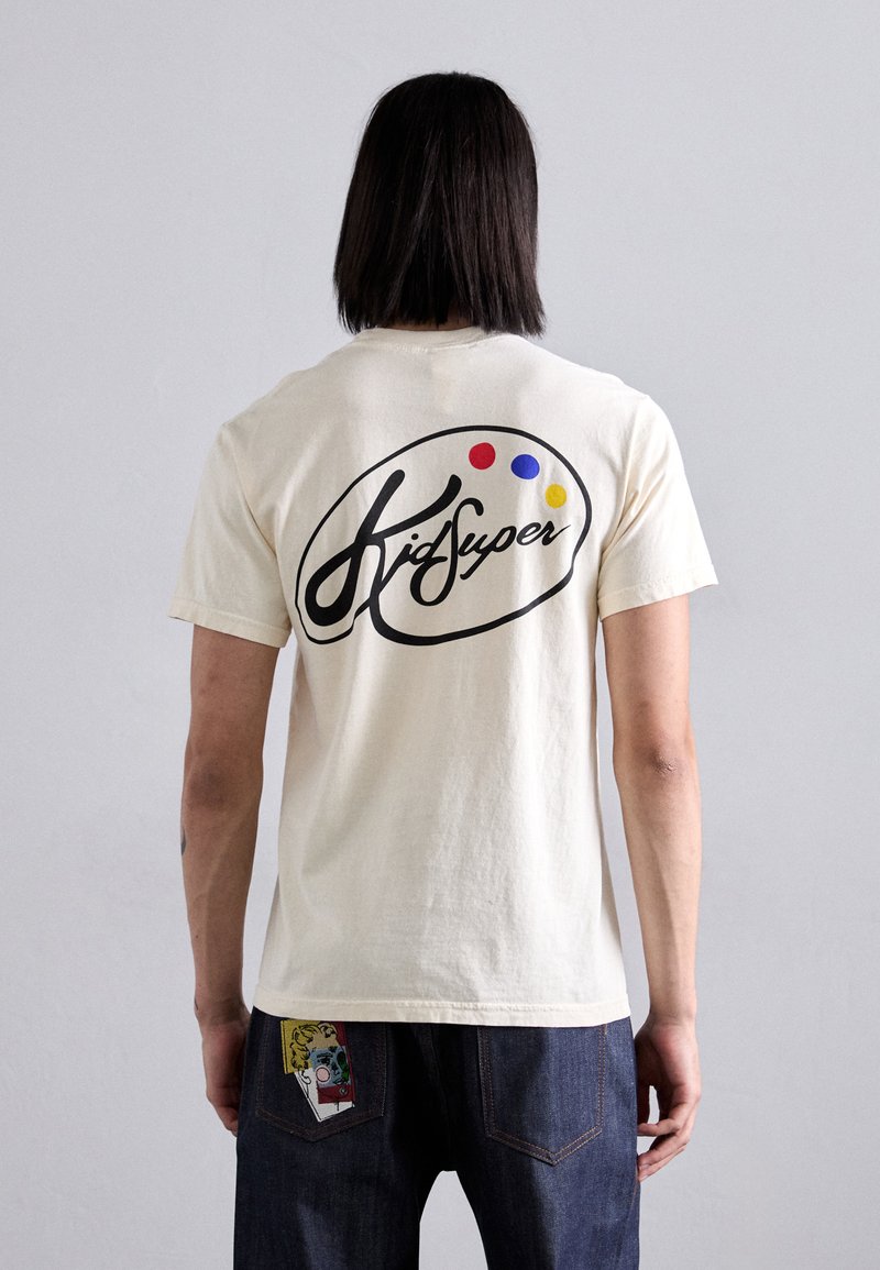 Cream-colored cotton t-shirt featuring a black logo with colorful dots on the back. Simple design, short sleeves, and relaxed fit.