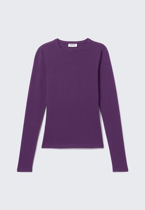 Lilla pikkade varrukatega ümar kaelusega särk, kitsas lõige, ilma mustrita, nähtava kaelamärgisega helehalli tausta peal.