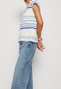 Pruhovaný top s krátkým rukávem v bílé, modré, žluté a růžové barvě. Spárováno s světle modrými širokými džíny. Casual střih, měkký bavlněný materiál.
