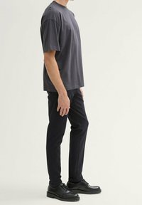 Grå kortärmad T-shirt med avslappnad passform, ihop parat med slim-fit mörkblå byxor och svarta snörskor. Släta texturer genom hela outfiten.