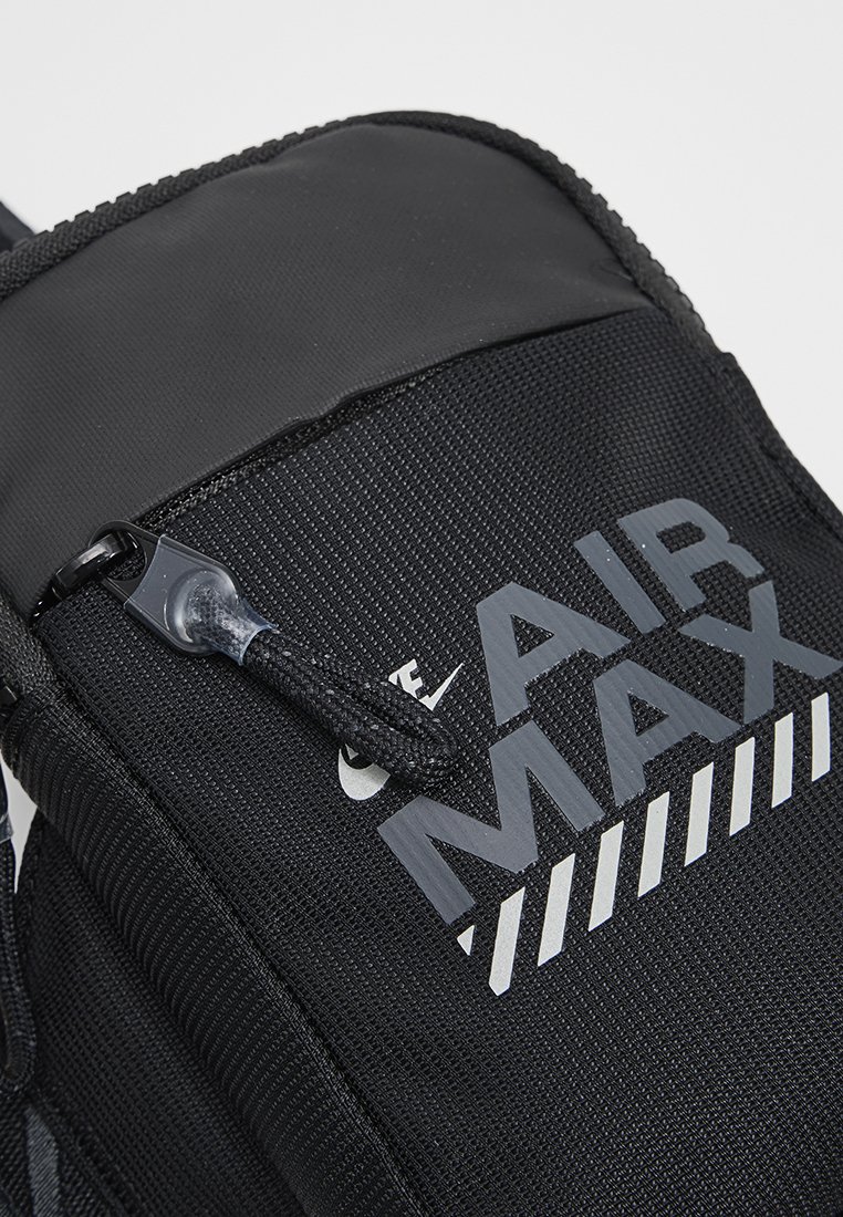 Mochila negra de nylon con un acabado texturizado, destacada marca "AIR MAX" en gris y un cierre con cremallera y tira de agarre.