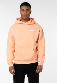 Kapuzensweatshirt in hellem Pfirsich mit einer vorderen Tasche. Mit weißem "WORLDWIDE"-Text auf der Brust. Weicher Stoff und lässige Passform.