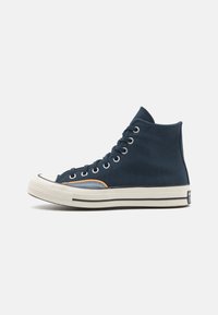 Høye sneakers i marineblå kanvas, med gummitåhette, hvit såle med svart stripe, samt blå og oransje detaljer på siden.
