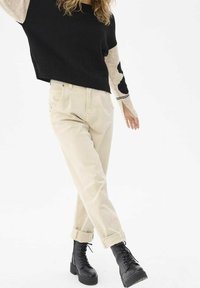 Pull noir et beige en tricot avec une manche à motif, associé à un pantalon beige clair fuselé et des bottes de combat noires à lacets.