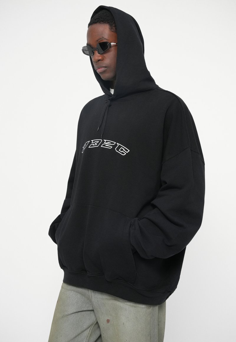 Zwarte hoodie met een voorzak en geborduurde tekst "1923C" in het wit. Ruime pasvorm met oversized mouwen en zachte stof.