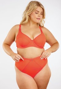 Punainen alusvaatesetti, jossa on ristikkäiset rintaliivit ja verkkoyksityiskohtia, yhdistettynä korkeavyötäröisiin alushousuihin, joissa on geometrisia kuvioita ja sileä pinta.