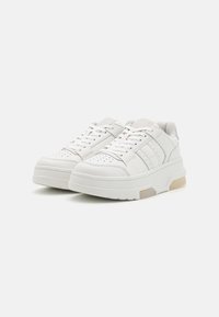 Valkoiset nahkakengät, joissa on teksturoitu pinta, varustettu rei'illä, litteillä nauhoilla ja pehmeällä pohjalla. Sivukorostukset ja minimalistinen muotoilu.