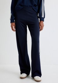 Navy wijde broek van een zachte stof, met zijstreepjes en een relaxte pasvorm, gecombineerd met witte sneakers.