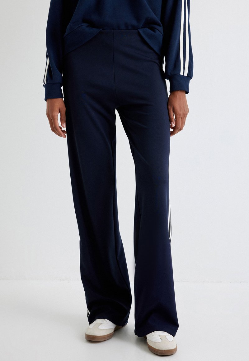 Navy wijde broek van een zachte stof, met zijstreepjes en een relaxte pasvorm, gecombineerd met witte sneakers.