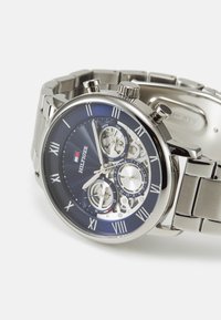 Montre en acier inoxydable avec un cadran bleu, des accents argentés, des chiffres romains, trois sous-cadrans et une finition polie. Dotée d'un bracelet à maillons.