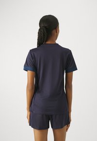 Marinblå træningsskjorte med korte ærmer og rund hals; tekstureret stof og kontrastfarvede ærmer; parret med matchende shorts.