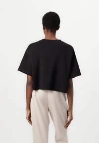 Black cropped t-shirt with short sleeves and a round neck; made of soft fabric. Worn with beige, loose-fitting pants.