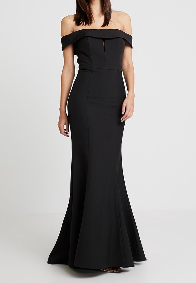Femme portant une robe de soirée noire ajustée, épaules dénudées, silhouette sirène sur un fond neutre.