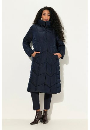 Long navy puffer coat with a high collar, featuring a quilted design and side pockets, paired with dark pants and heeled boots.