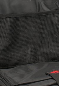 Poche en filet noir et compartiment en tissu pliable à l'intérieur d'un sac avec un logo rouge sur une sangle noire.