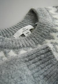Maglione grigio con scollo a costine, caratterizzato da una texture morbida e un motivo geometrico bianco. Etichetta visibile con la scritta "THE SET, MADE IN CHINA, AGE."