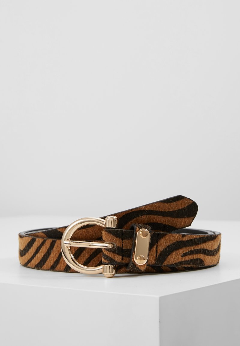 Ceinture marron et noire à rayures tigre avec une boucle circulaire dorée reposant sur une surface blanche sur fond uni.