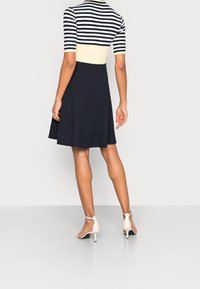 Šaty bez ramínek s pruhovaným černobílým topem a přiléhavou námořnickou sukní. Hladká tkanina, rozšířený tvar, doplněné béžovými lodičkami na kotníku.