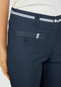 Marineblaue Hose aus leichtem Stoff mit einer seitlichen Reißverschlusstasche, zwei weißen Streifen am Bund und einer silbernen Knopfschließe.