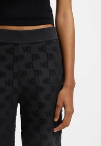 Sorte joggebukser med et blødt, tekstureret stof og et præget gentaget logomønster, suppleret med en bred elastisk talje.