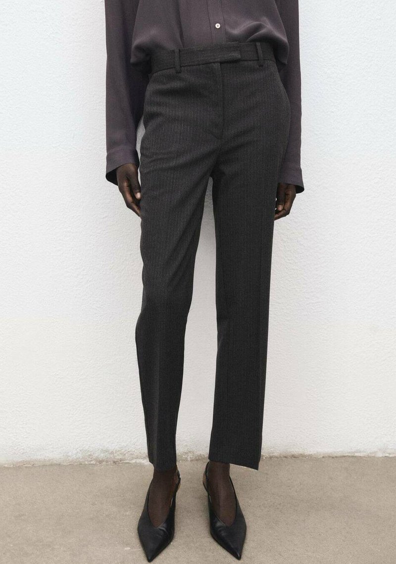 Pantalon sur mesure gris foncé à fines rayures, coupe droite, avec une ceinture avant, accompagné de talons pointus noirs assortis.