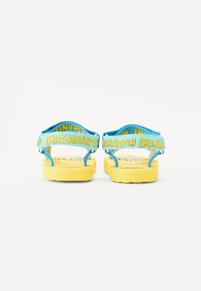 Gele flip-flops met blauwe banden waarop het woord "IMAGINAATION" in geel is gedrukt. Dikke, gegroefde zolen met een speels ontwerp.