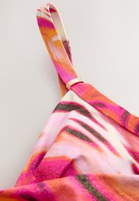 Tissu à motif floral, aux teintes vives de rose, orange et or. Bretelle réglable avec détail en métal doré à l'épaule.