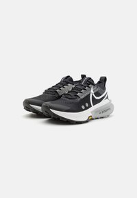Black athletic shoes with a textured upper, grey accents, white branding, and a thick white midsole featuring a yellow logo.