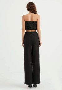 Black two-piece outfit featuring a strapless top and high-waisted, wide-leg pants with a textured fabric and elastic waistband.