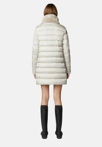 Lichtgekleurde gewatteerde jas met een hoge bontkraag, voorzien van doorgestikte secties en een lengte tot halverwege de dij, gecombineerd met zwarte hoge laarzen tot aan de knie.