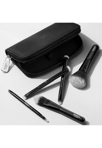Zestaw czarnych pędzli do makijażu KIKO wyeksponowanych z czarną, teksturowaną saszetką na zamek. Pędzle różnią się kształtem i rozmiarem, posiadając miękkie włosie oraz smukłe rączki.
