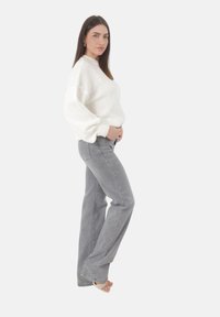 Suéter blanco de punto con cuello alto y mangas abullonadas, combinado con jeans acampanados en gris claro y tacones destalonados en tono nude.