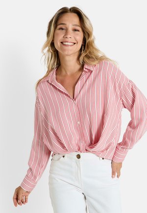 Chemise à boutons rouge et blanche à rayures, à manches longues, coupe décontractée, avec un détail noué à l'avant, assortie à un pantalon blanc taille haute.