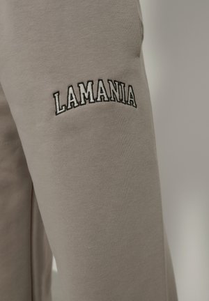 Sivé tepláky s vyšitým logom "LAMANIA" na ľavom stehne. Tkanina sa zdá byť hladká s mierne elastickou textúrou.