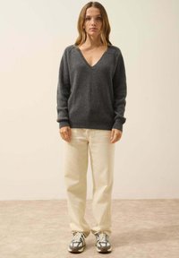 Szary sweter w serek o prążkowanej fakturze, zestawiony z jasnobeżowymi spodniami i casualowymi trampkami. Prosty design, luźny krój.