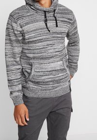 Sudadera con capucha de rayas grises y negras, con cuello alto, cordones ajustables, bolsillos delanteros y puños acanalados. Fabricada con tejido de punto texturizado.