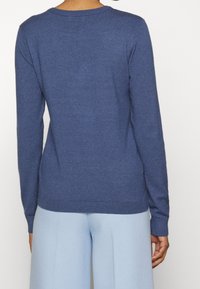 Modrý pletený svetr s dlouhými rukávy a kulatým výstřihem. Texturovaná tkanina, žebrované manžety a spodní lem. Pohled zezadu ukazuje hladkou siluetu.